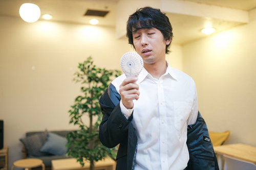 オフィスの冷房が壊れて手持ち扇風機で涼む男性