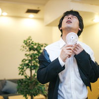 首元の汗を乾かすビジネスマン、白いハンディ扇風機で暑さ対策の写真