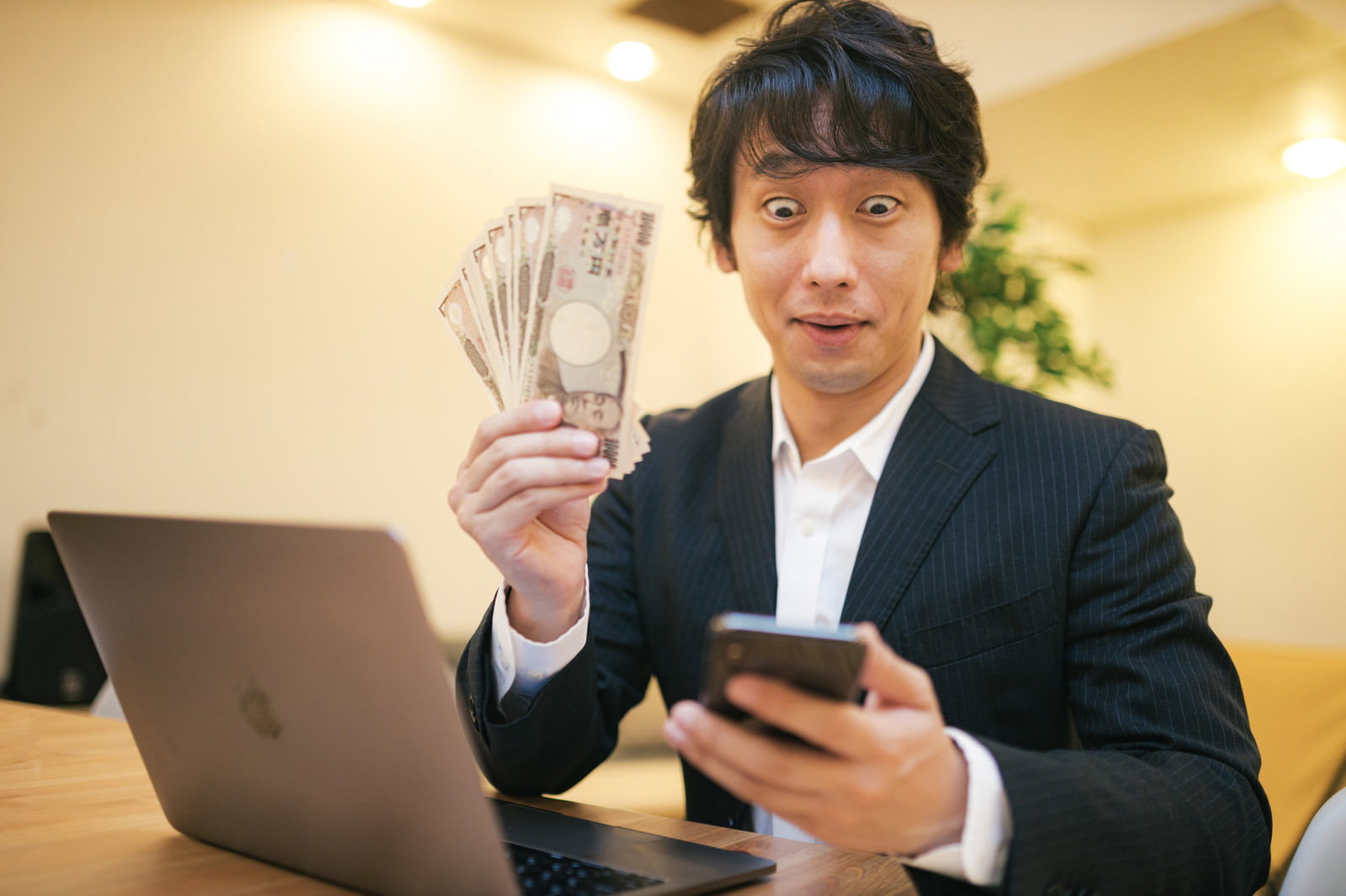 お札を手に持ち笑顔で喜んでいるスーツ姿の男性［モデル：大川竜弥］