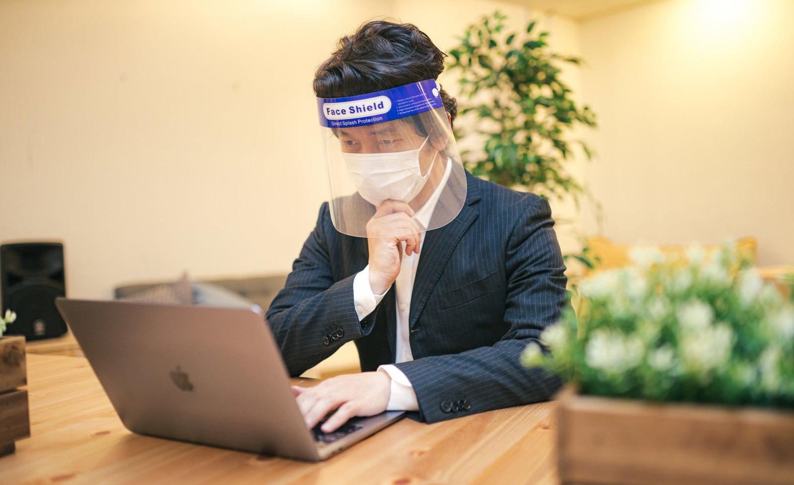 フェイスシールドを着けてノートパソコンで作業するスーツ姿の男性［モデル：大川竜弥］