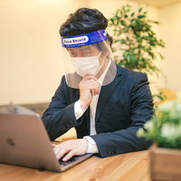 フェイスシールドを装着してデスクワークする男性の写真
