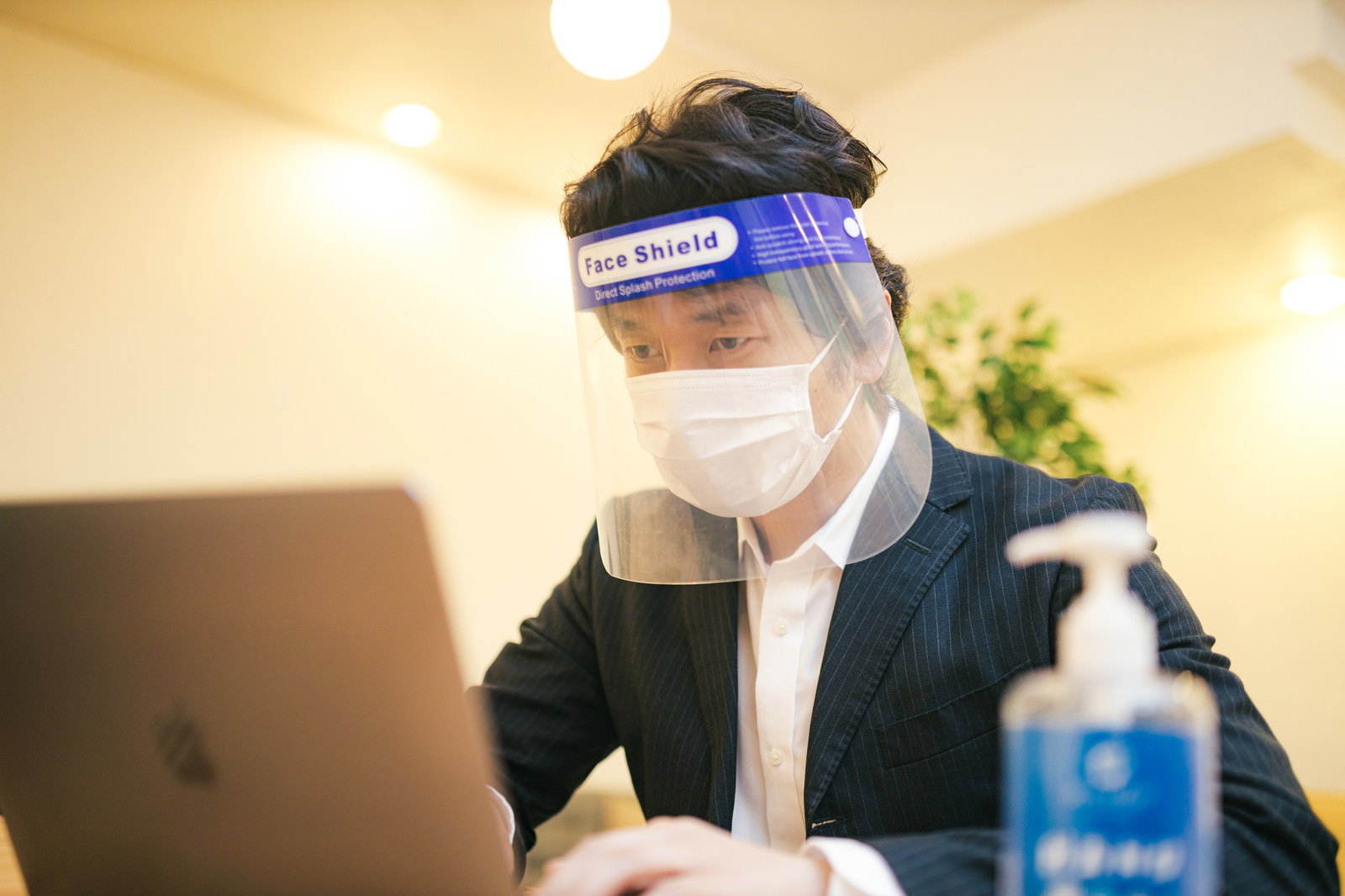 フェイスシールドとマスクを装着してパソコンを使用する男性［モデル：大川竜弥］
