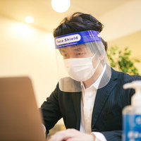 オンライン会議中もフェイスシールドとマスクを装着する男性の写真