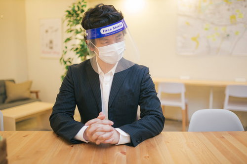 フェイスシールドとマスクを装着した男性がビジネススーツで会議室に座る