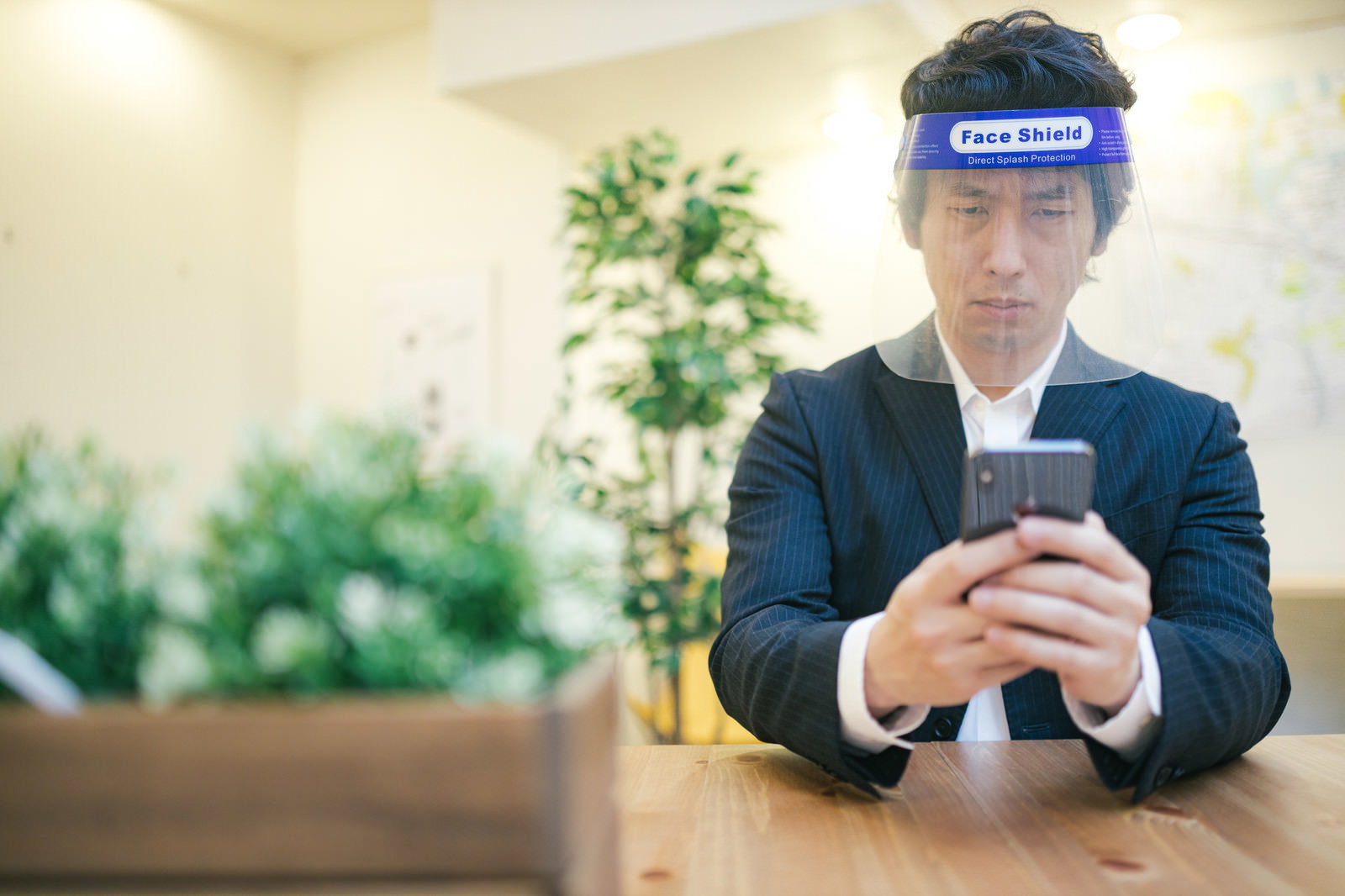 フェイスシールドを装着してスマホを操作する会社員［モデル：大川竜弥］