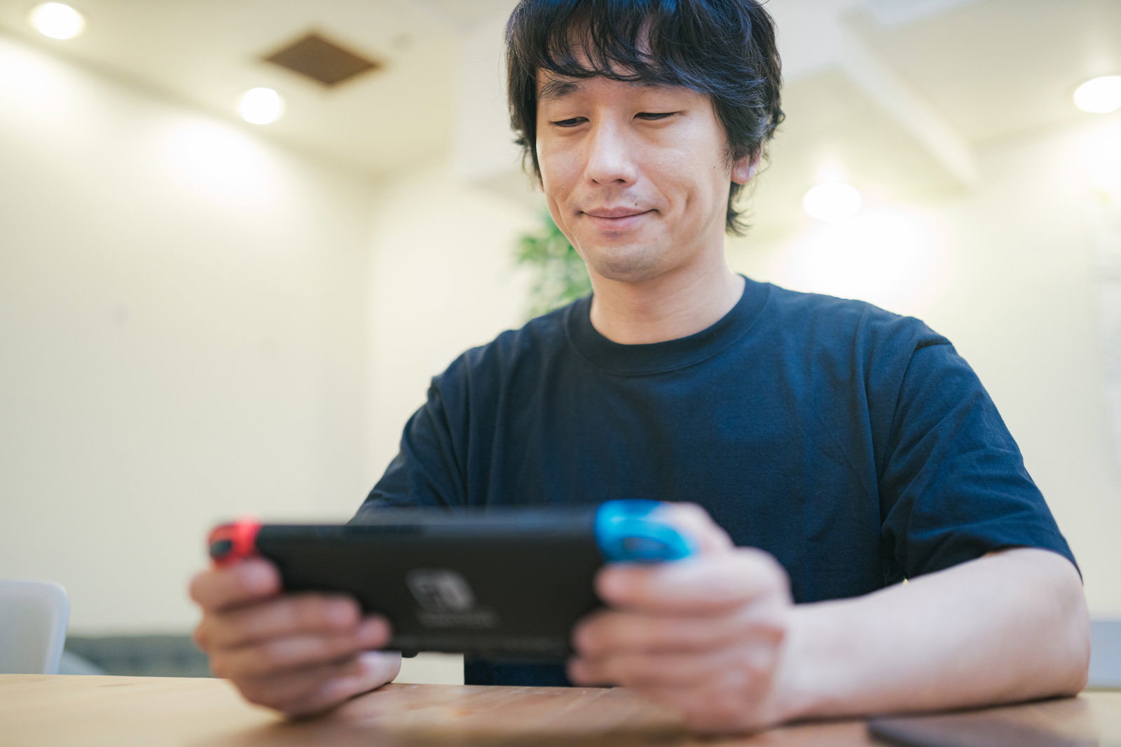 黒いTシャツを着た男性が携帯ゲーム機を操作している様子［モデル：大川竜弥］