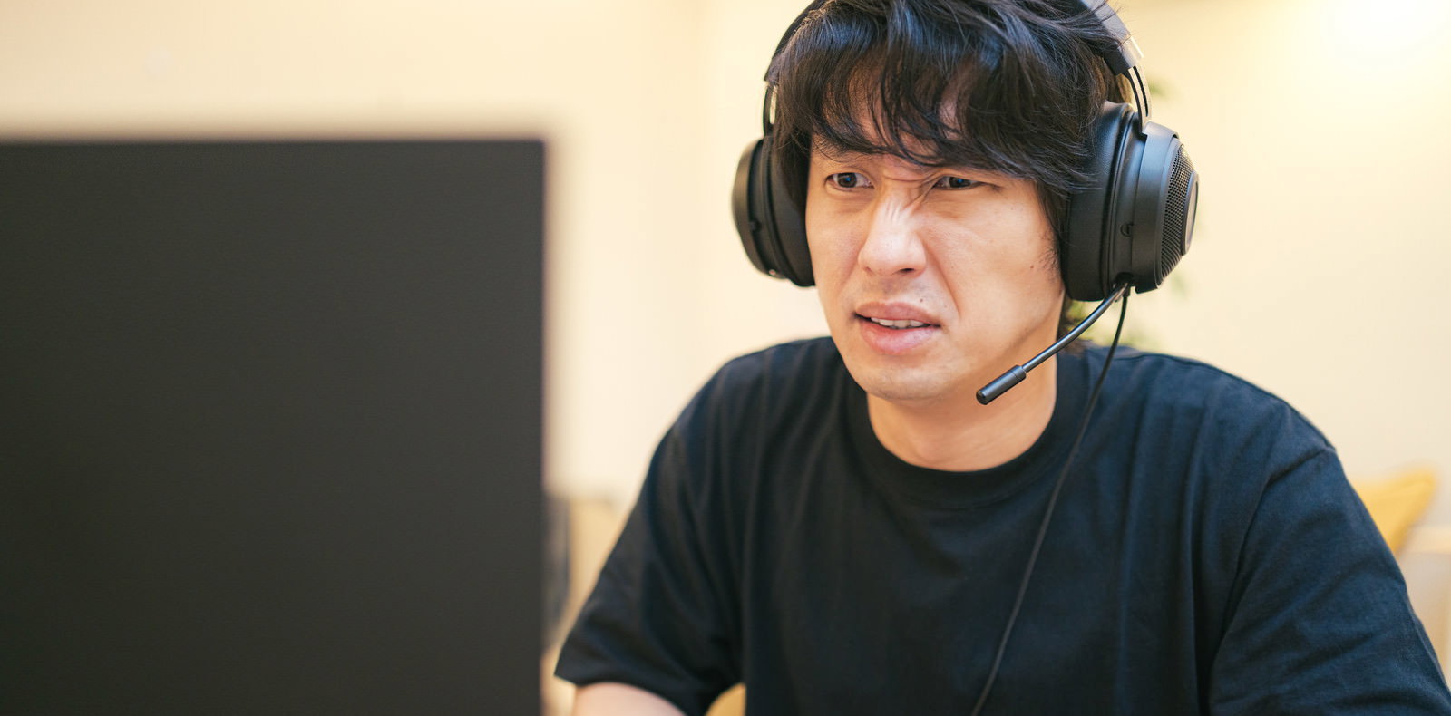 ヘッドセットを付けてイライラしながらゲームする男性［モデル：大川竜弥］
