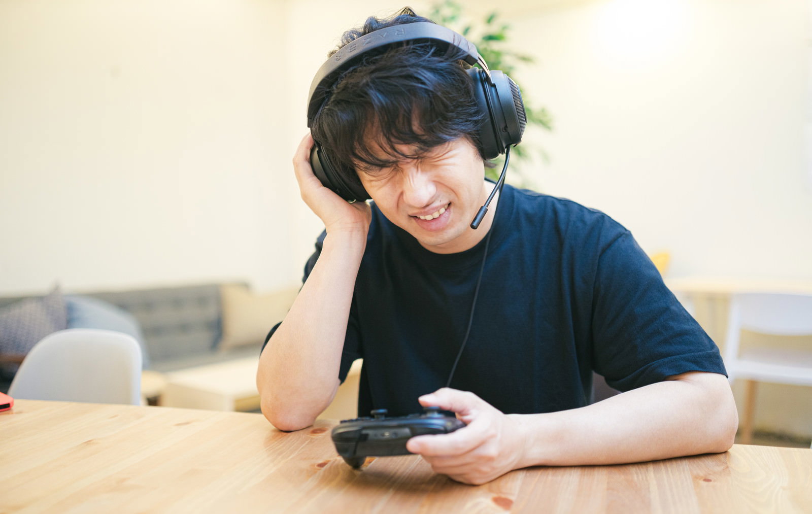 頬杖をついてスマートフォンを見つめる悔しそうな表情の男性ゲーマー［モデル：大川竜弥］