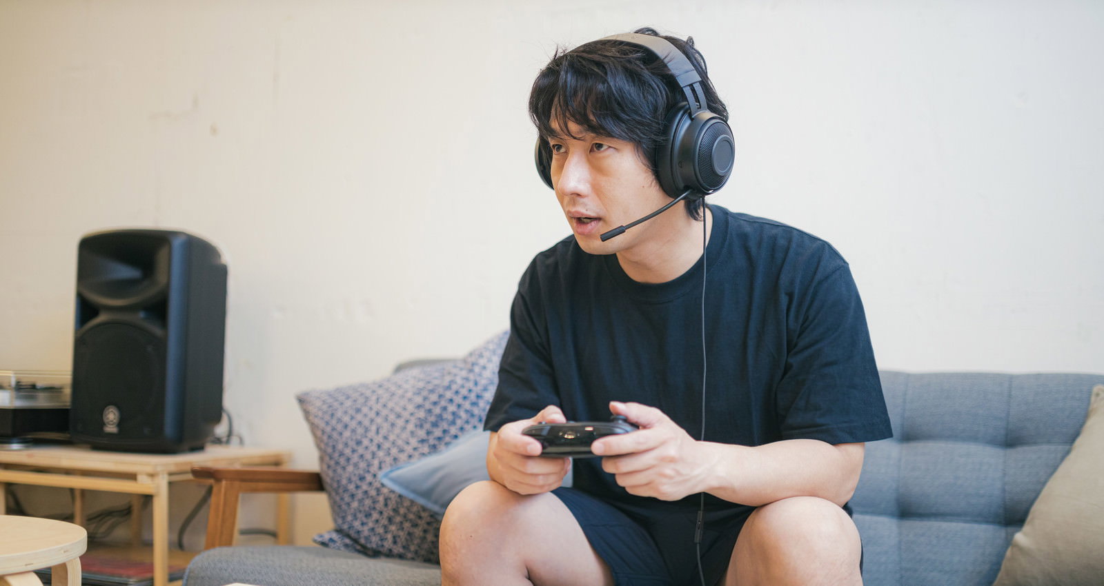ヘッドセットをつけてゲームコントローラーを持ちリビングでゲームする男性［モデル：大川竜弥］