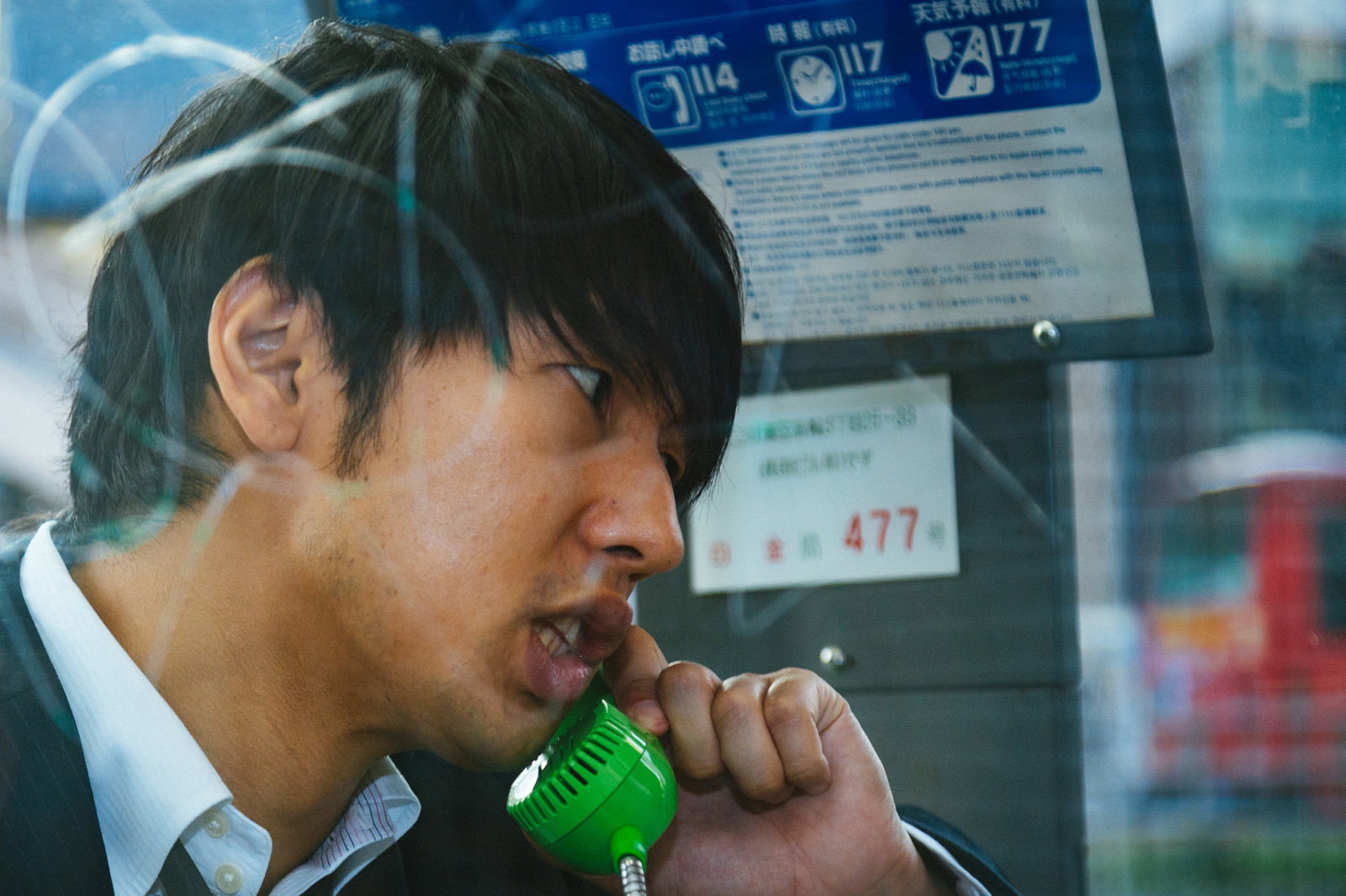 電話ボックスで緊張した表情で通話する男性［モデル：大川竜弥］