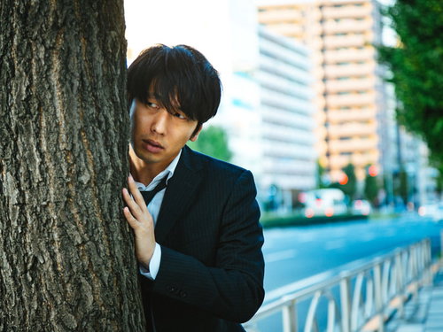 浮気調査で尾行中の探偵が木陰に身を隠して張り込む