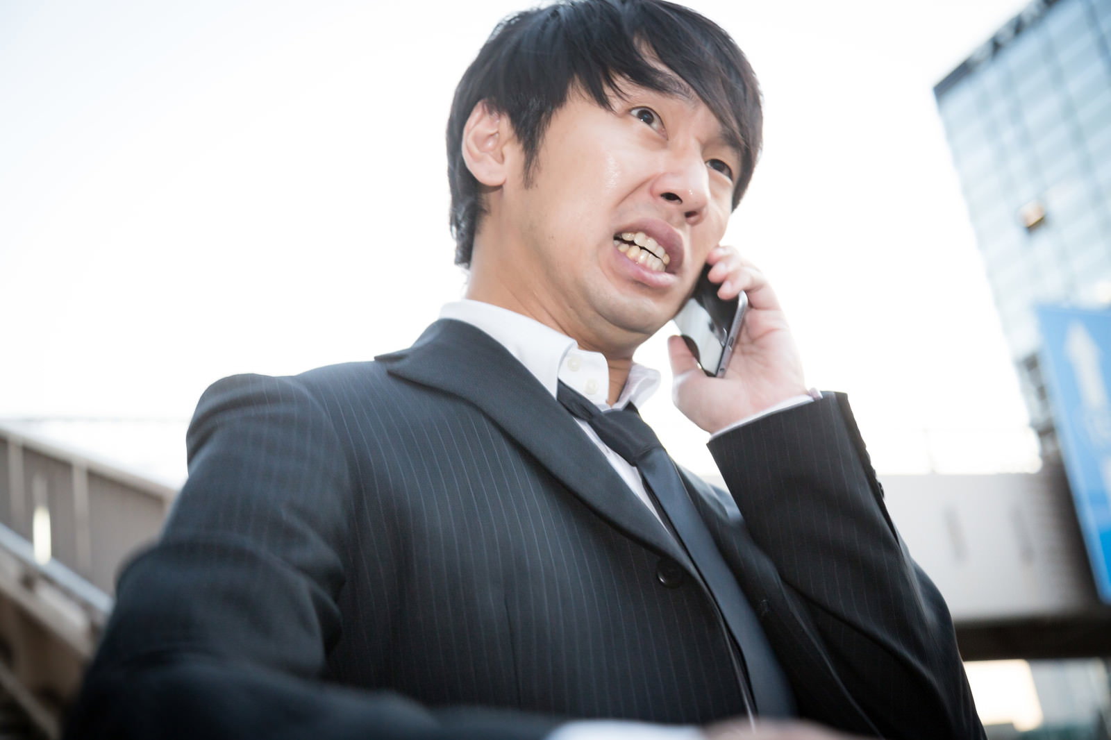 グレーのスーツを着た男性が携帯電話で通話しながら慌てて走っている［モデル：大川竜弥］