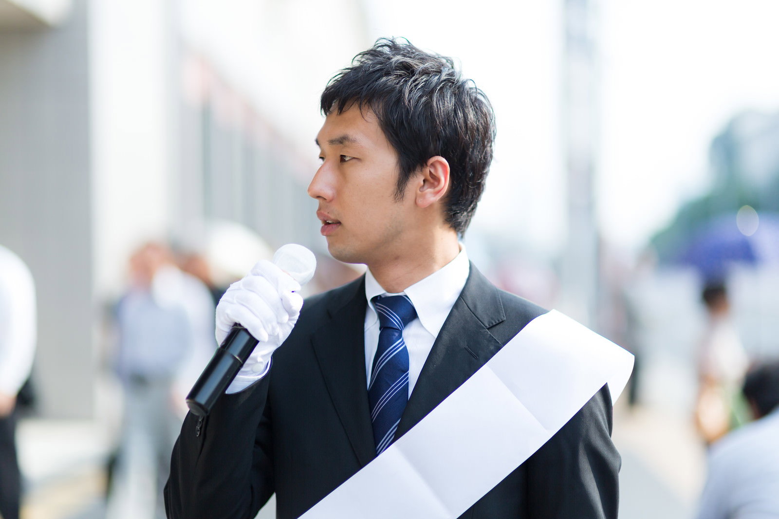 マイクを持って街頭演説をするスーツ姿の男性［モデル：大川竜弥］