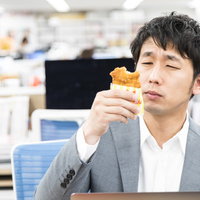 オフィスの昼食でファミチキを食べるスーツ姿の男性の写真