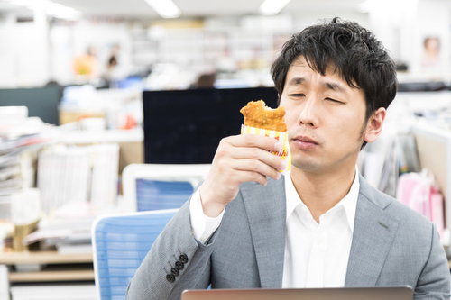 オフィスの昼食でファミチキを食べるスーツ姿の男性