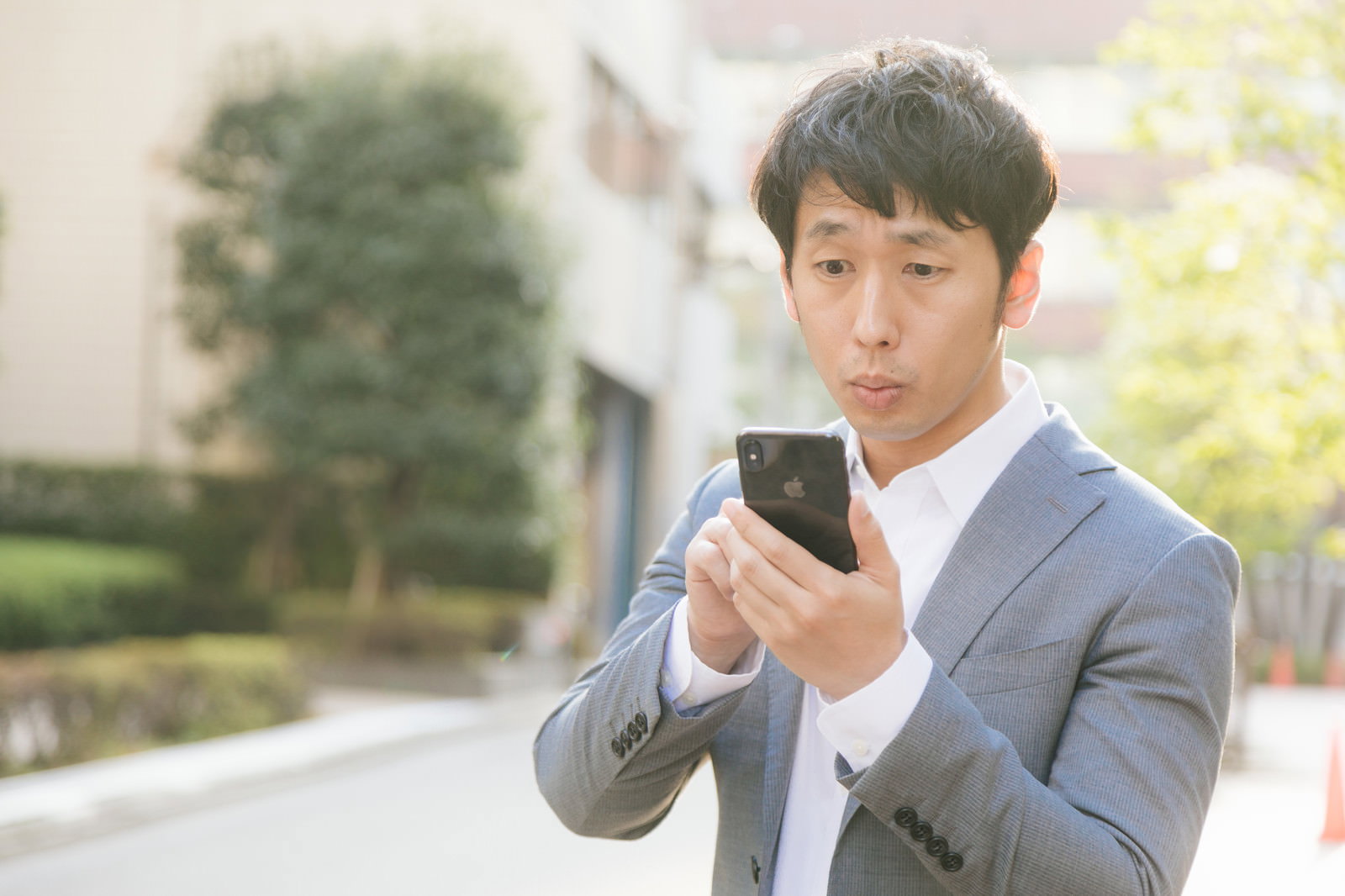屋外でスマートフォンを操作するグレーのスーツを着た会社員男性［モデル：大川竜弥］