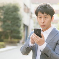 新作アプリのチェックに余念がないスマホを操作する会社員男性の写真