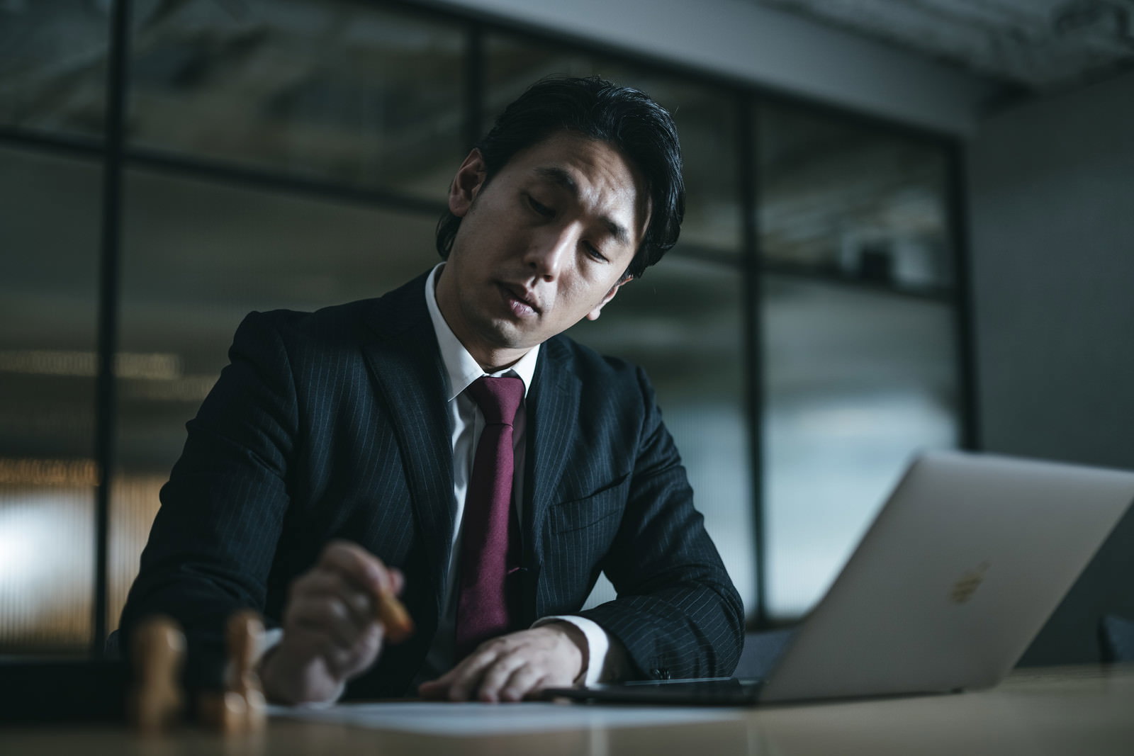 深夜のオフィスで契約書に判子を押しているスーツ姿の男性［モデル：大川竜弥］