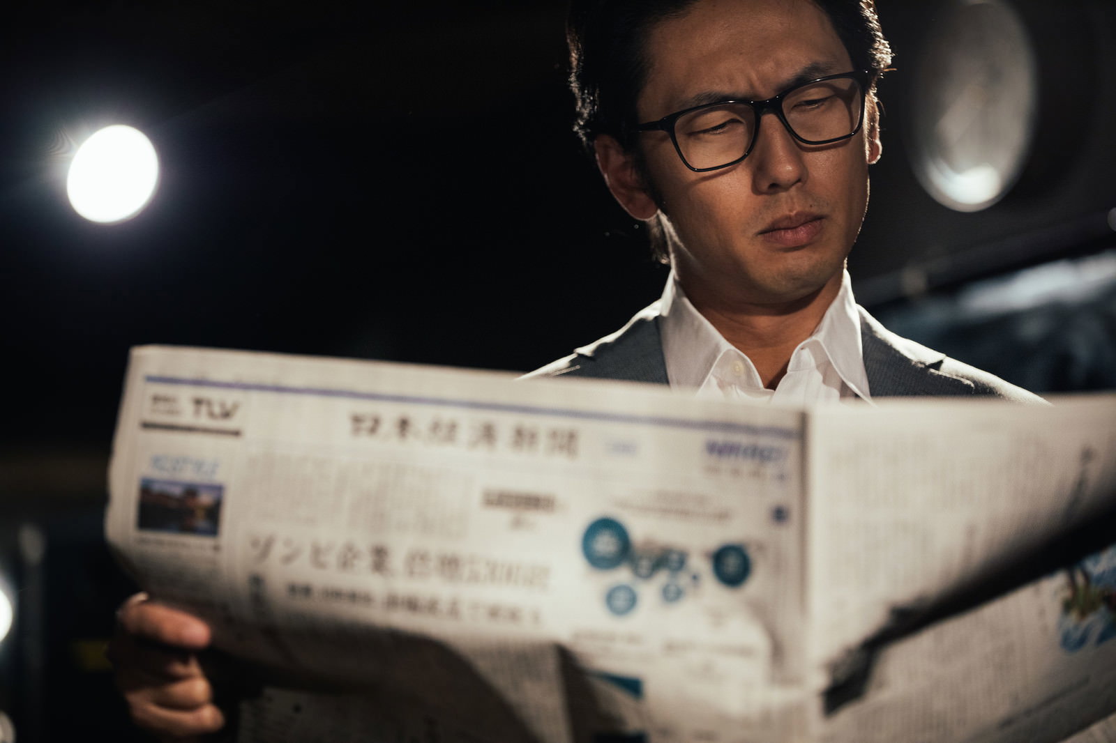 眼鏡をかけたビジネスマンが経済新聞を広げて読んでいる様子［モデル：大川竜弥］