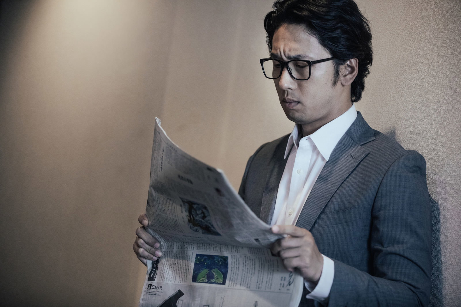 グレーのスーツを着た眼鏡の男性が新聞を読んでいる［モデル：大川竜弥］