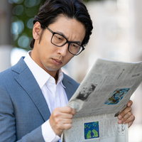 目を凝らして紙面を読む会社員、株価情報を確認の写真