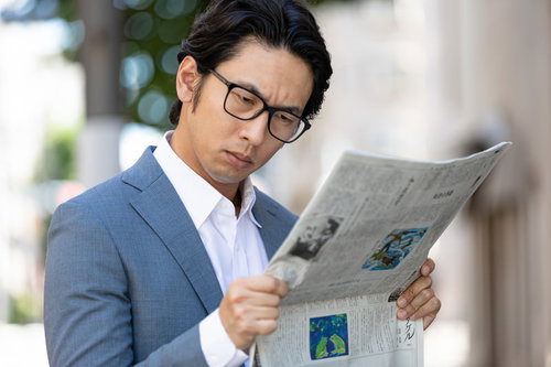 目を凝らして紙面を読む会社員、株価情報を確認