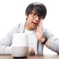 スマートスピーカーに向かって呼びかけるメガネ姿の男性の写真