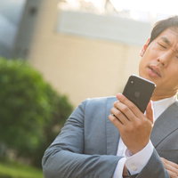 暴落して追証発生・・・困った顔でスマホを見つめる会社員の写真
