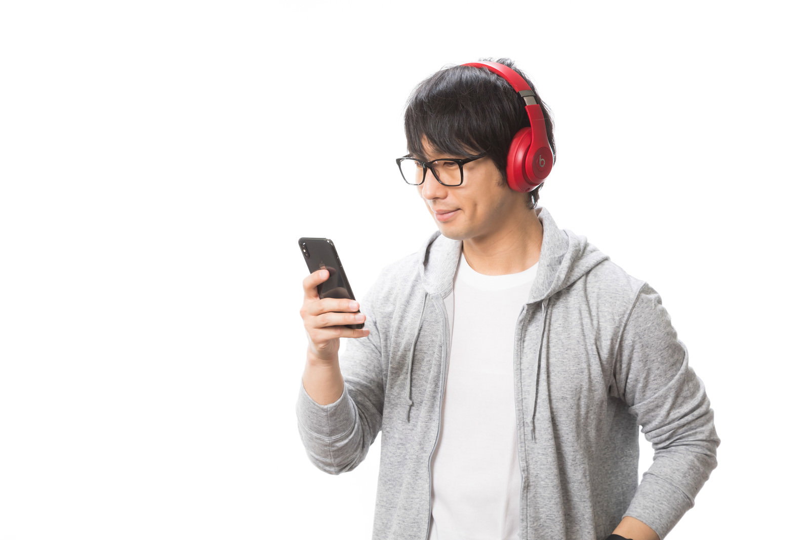 赤いワイヤレスヘッドホンを装着してスマートフォンを操作する男性［モデル：大川竜弥］