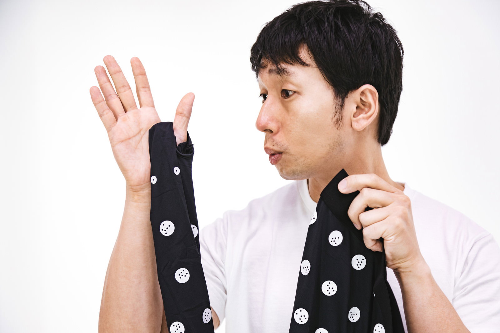 黒い水玉模様のネクタイを手に持ち、ポーズを取る男性［モデル：大川竜弥］