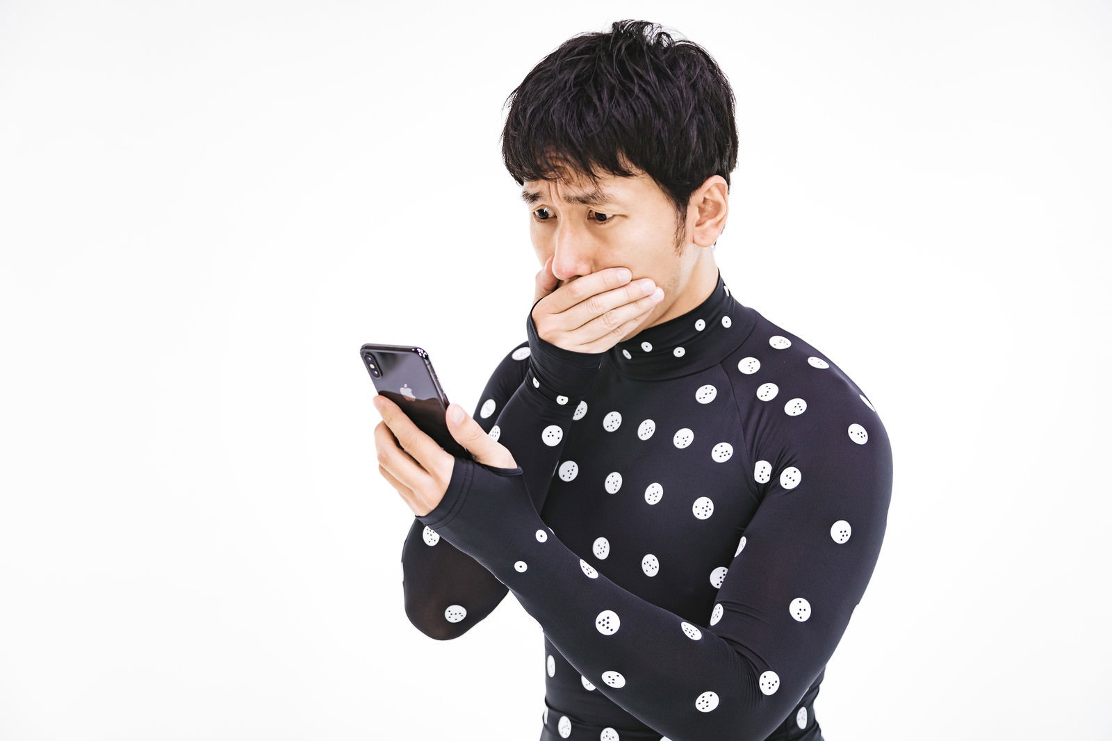黒いドット柄のボディスーツを着た男性がスマートフォン画面を見て口を覆い驚く［モデル：大川竜弥］