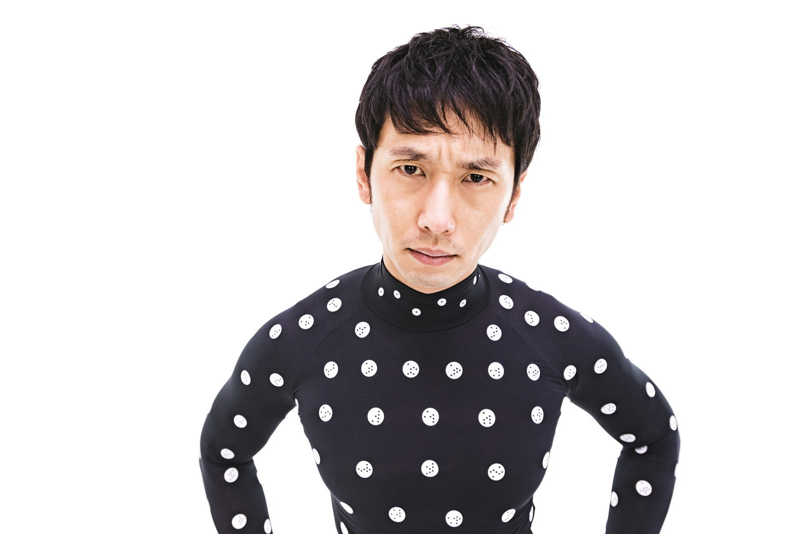 黒いドット柄の服を着て腰に手を当て睨む男性［モデル：大川竜弥］