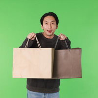 緑バックで両手に買い物袋を持つ黒Tシャツ姿の男性の写真
