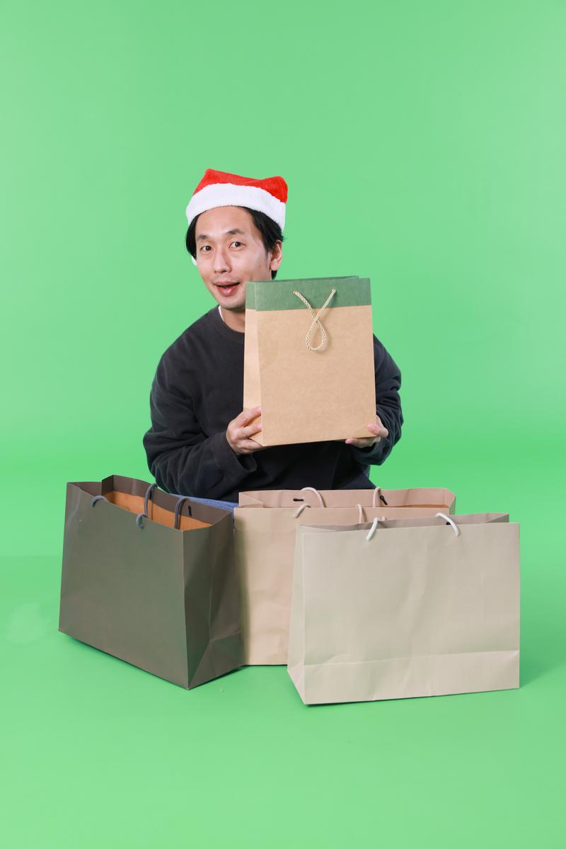 サンタ帽をかぶった男性が買い物袋を抱えて喜んでいる［モデル：大川竜弥］