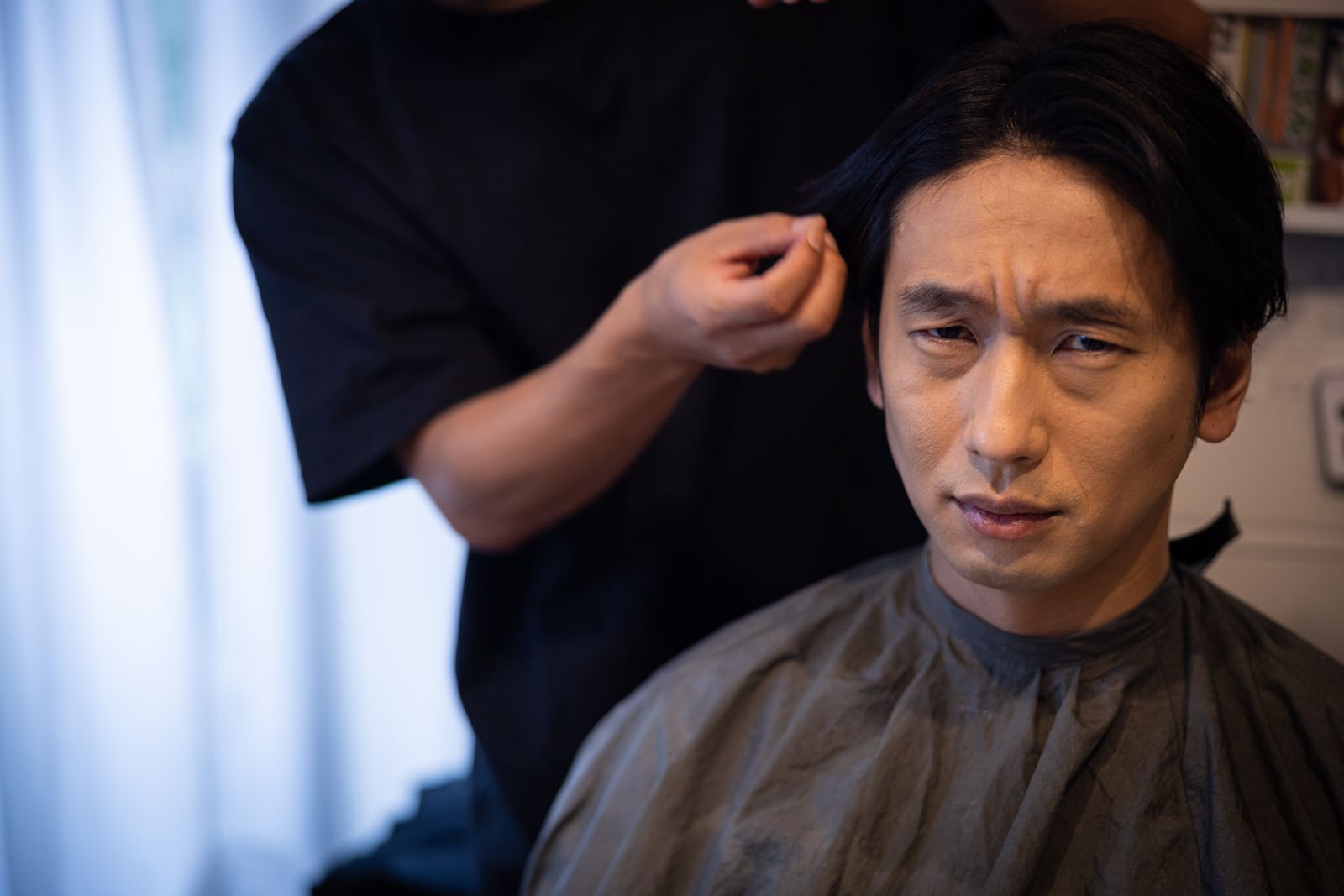 美容室で黒いケープを着用してヘアセットを受けている男性［モデル：大川竜弥］
