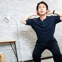 自宅で紺色のウェアを着てスクワットをする男性の写真