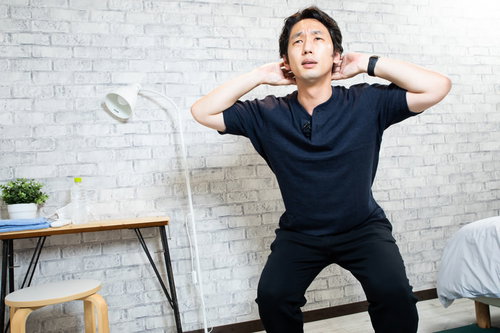 自宅で紺色のウェアを着てスクワットをする男性