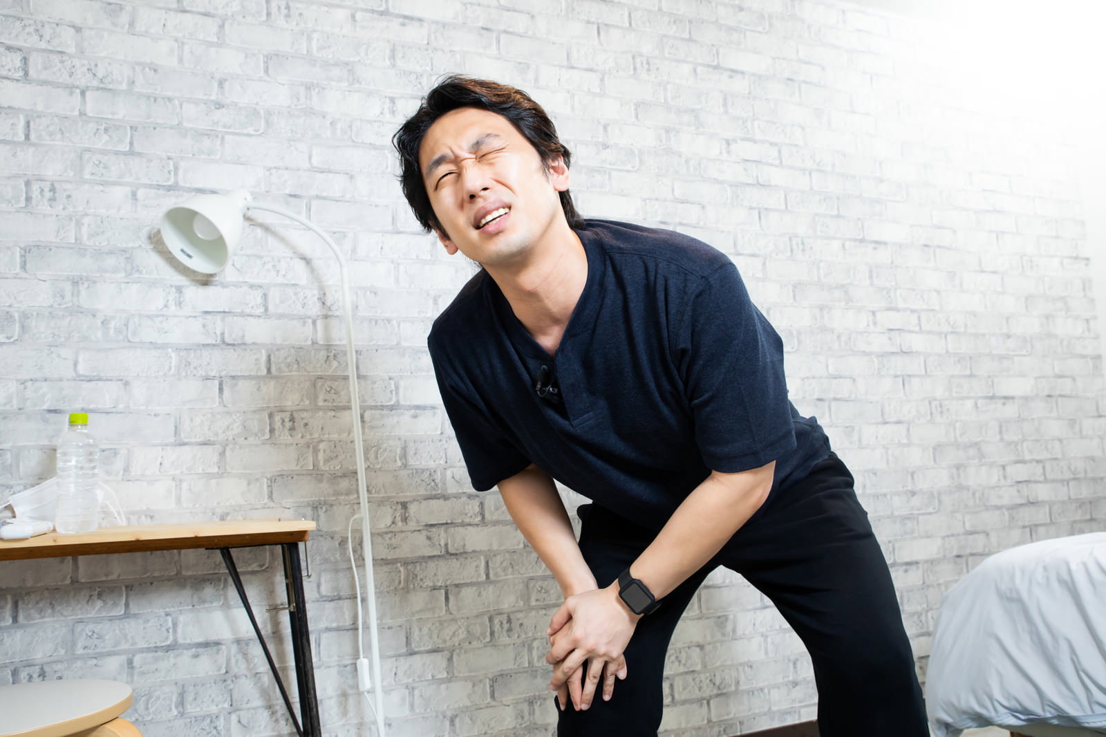 膝に手を当てて痛みを訴える黒いシャツの男性［モデル：大川竜弥］