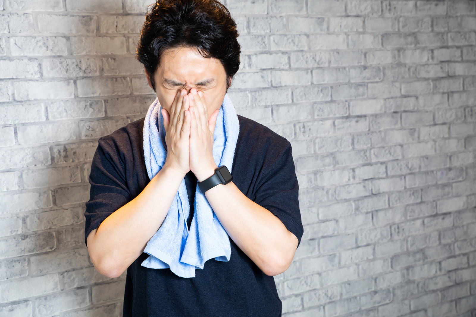 トレーニング後に疲労した表情で手で顔を覆う男性［モデル：大川竜弥］