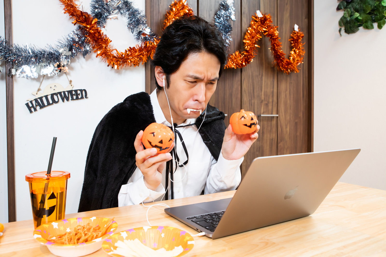 ハロウィン装飾の部屋でパソコンに向かってポーズを決める仮装した男性［モデル：大川竜弥］