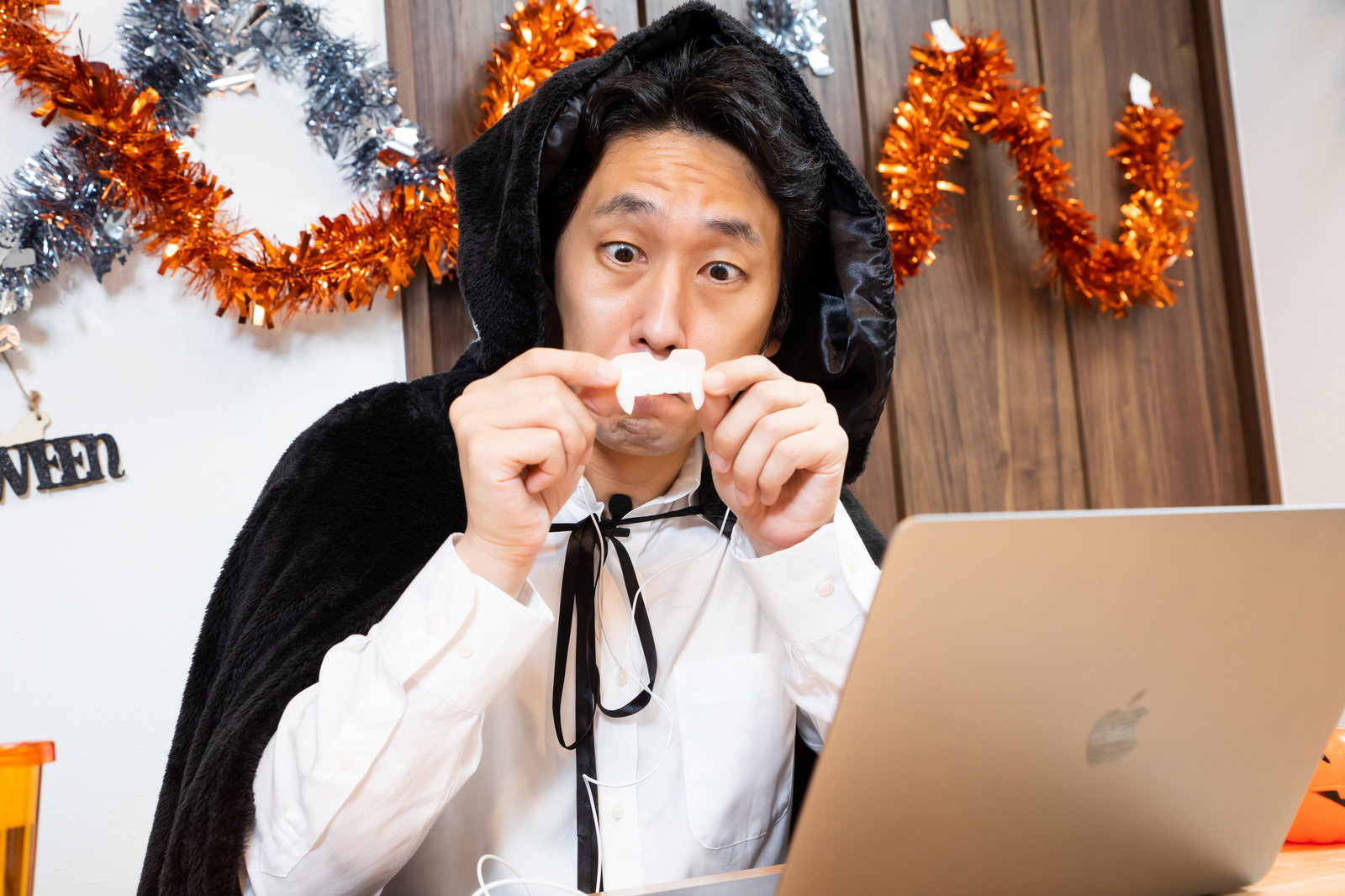 ハロウィン用のドラキュラの牙を準備する白いフード付き衣装の男性［モデル：大川竜弥］