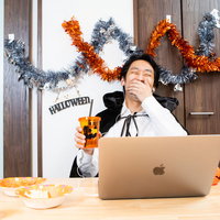 ハロウィンの仮装でノートパソコンを使ってリモート飲み会に参加する男性の写真