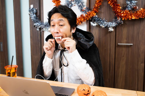 ドラキュラの仮装で張り切ってハロウィンのリモート飲み会の準備をする男性