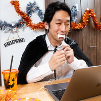 ハロウィンの仮装で黒いマントを羽織り、ノートパソコンでオンライン通話する男性の写真