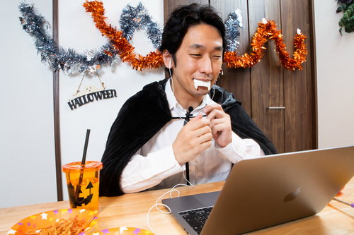 ハロウィンの仮装で黒いマントを羽織り、ノートパソコンでオンライン通話する男性