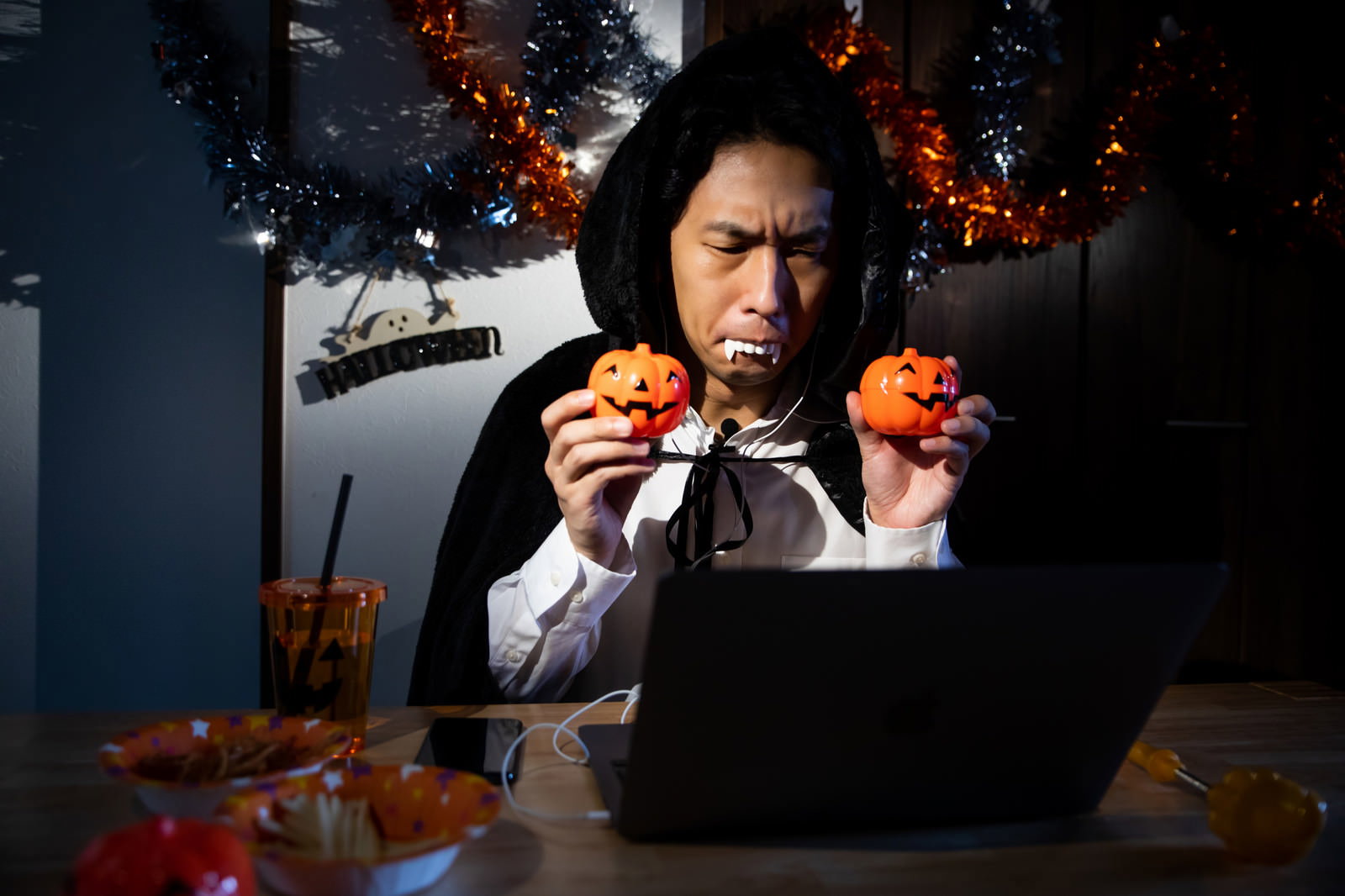 ハロウィンのドラキュラ仮装でノートパソコンを使ってリモート飲み会をする男性［モデル：大川竜弥］