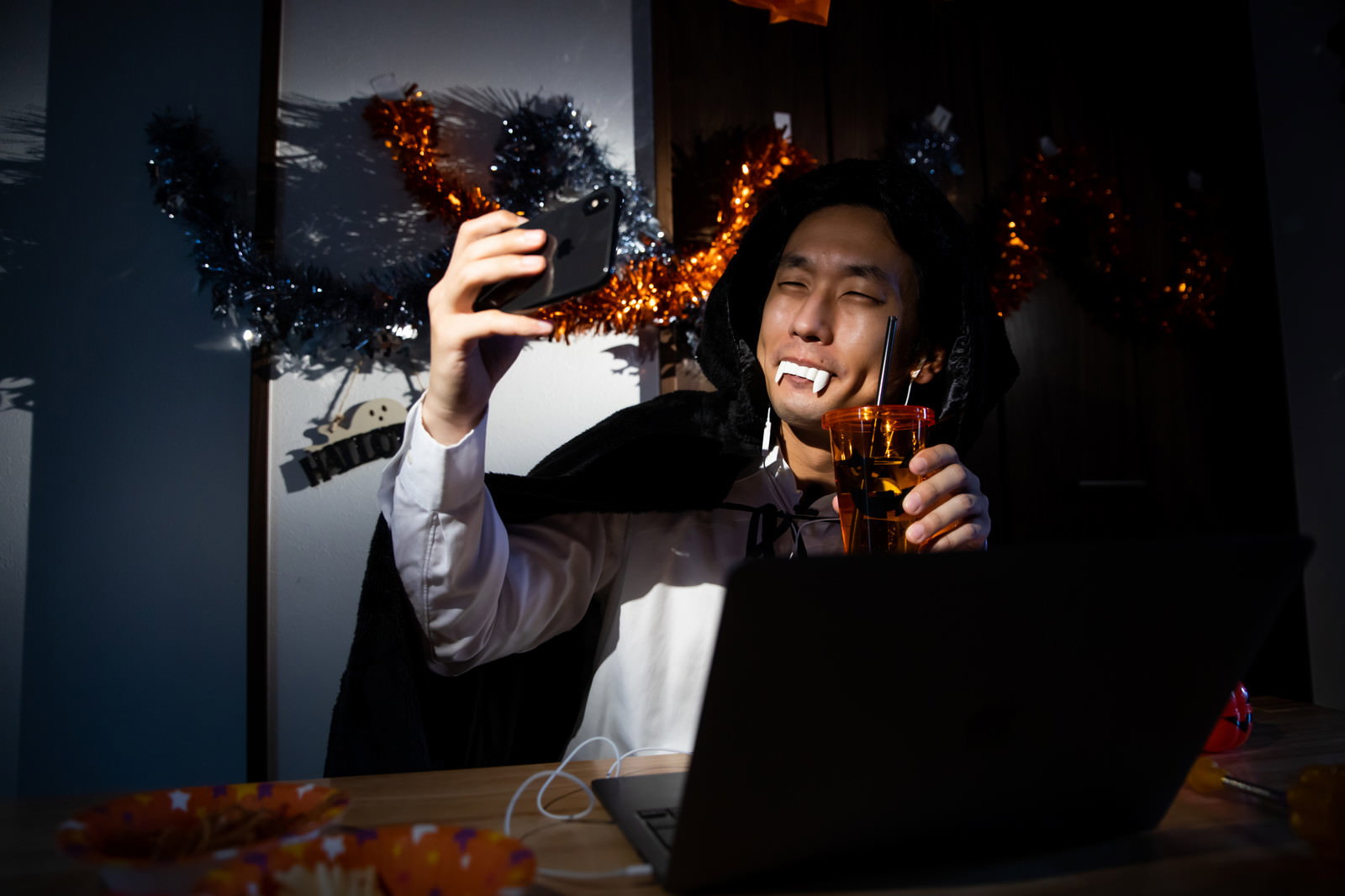 ドラキュラのコスプレをした男性がノートパソコンでオンライン飲み会を楽しんでいる［モデル：大川竜弥］