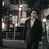 繁華街を歩くスーツ姿の男性とマスク女子のカップルの写真