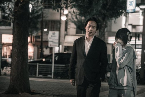 繁華街を歩くスーツ姿の男性とマスク女子のカップル