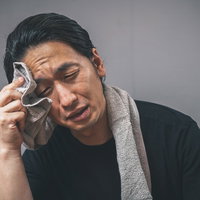 タオルで汗を拭う体調不良の男性の写真
